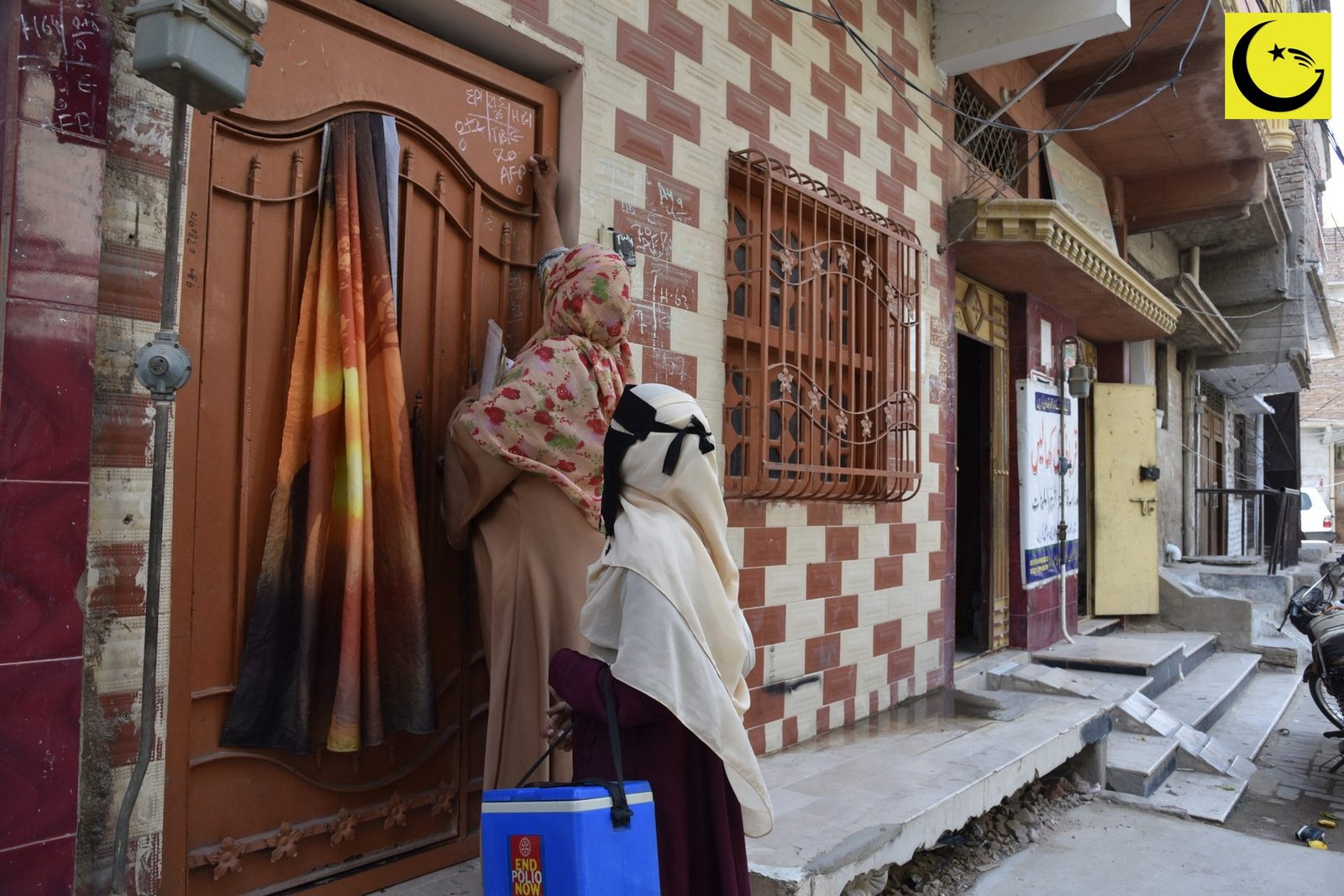 Pakistan polio cases 2026: a polio worker marks a door in Hyderabad, Sindh, after a house visit during the May 2026 vaccination campaign, vaccine carrier beside her